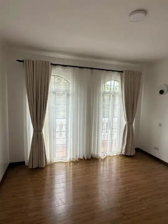 Neutral curtains tied back around sheer panels above a warm timber floor.