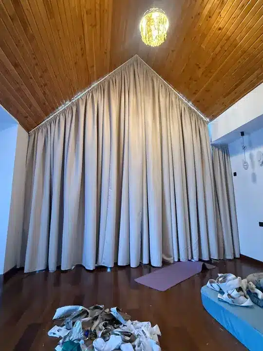 Curtains follow a dramatic pitched roofline beneath a timber ceiling, photographed during fitting.