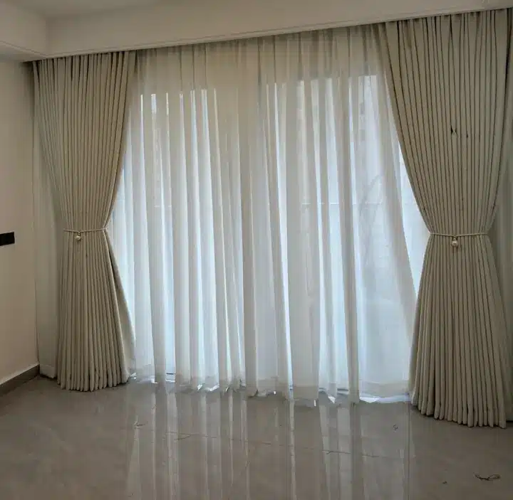 Cream curtains and white sheers across a broad opening, finished with symmetrical tiebacks.